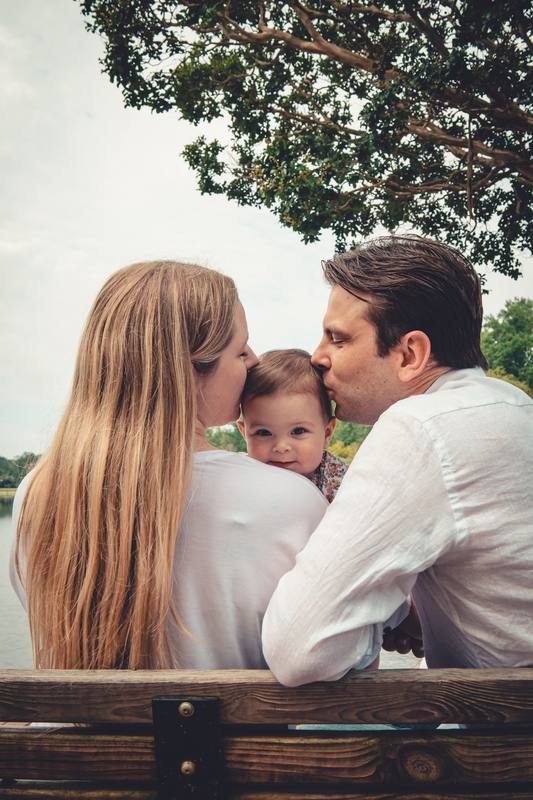 Parents kissing their baby on a park bench