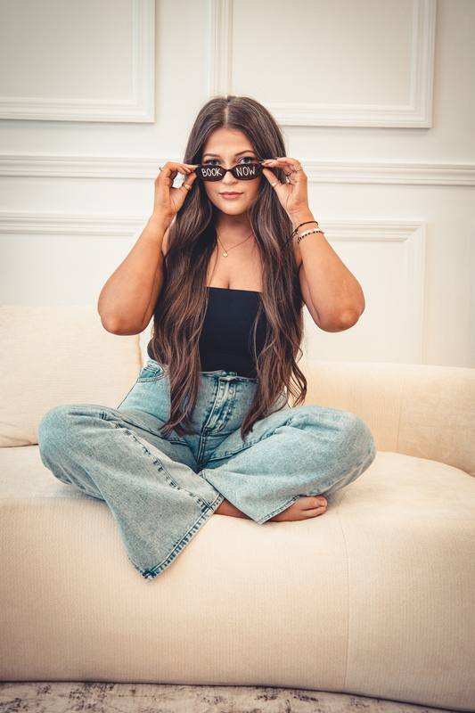 Woman in sunglasses sitting cross-legged on a cream sofa